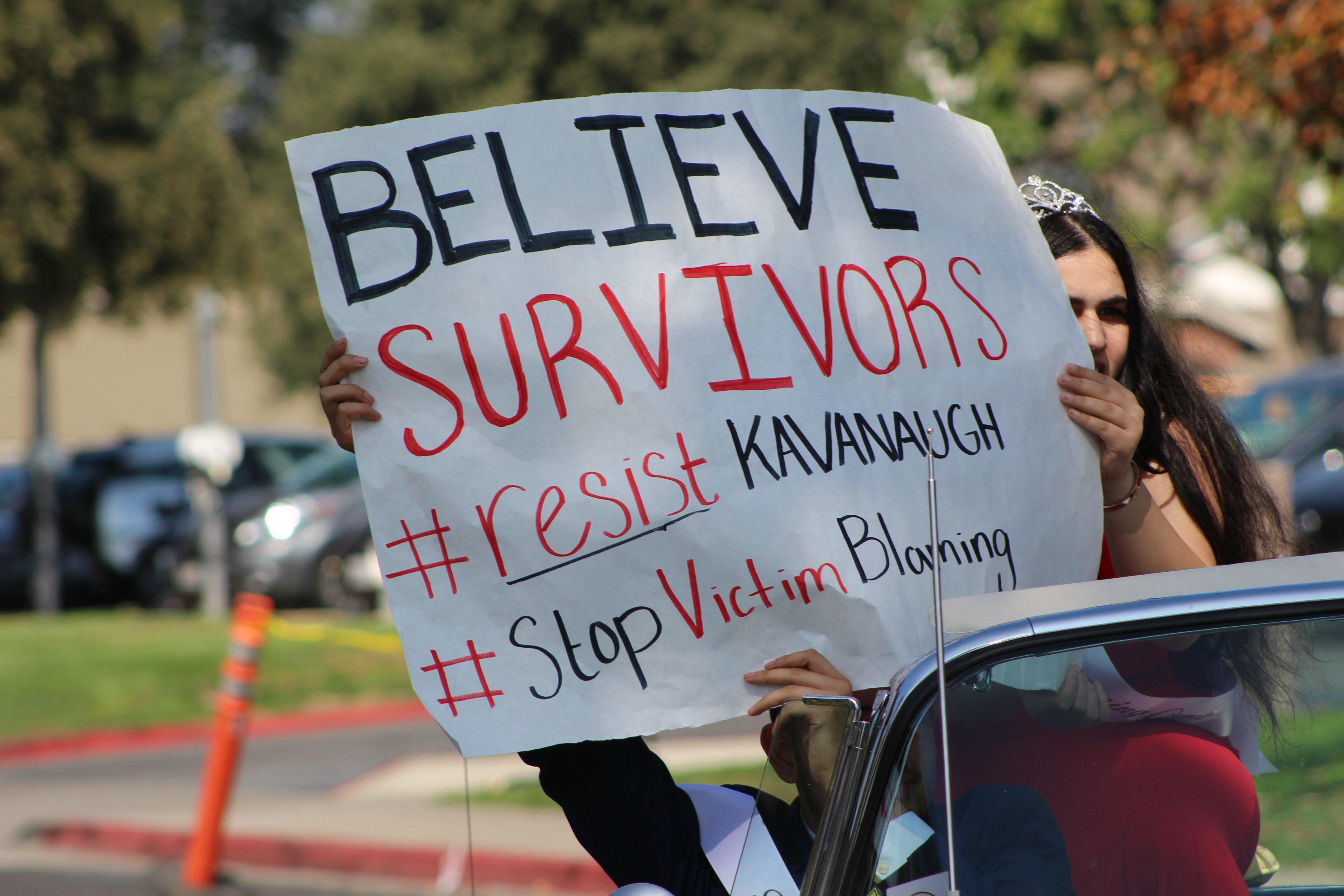Marco Torres holds poster that reads "Believe Survivors" inside the car during the homecoming procession. Photo by Nisha Malley.